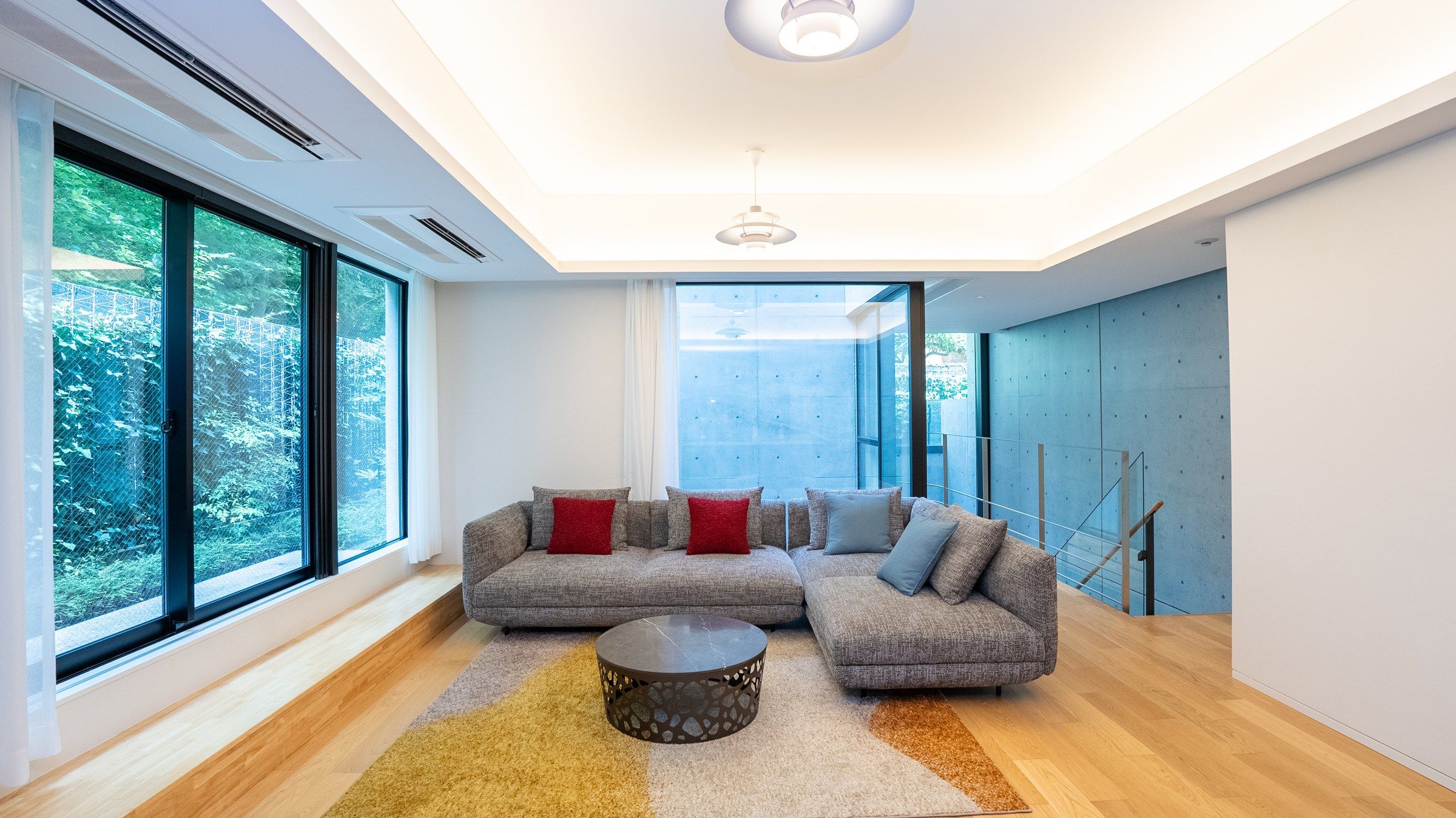 The living room of Hillpeak: a sofa before board-marked concrete seen through full-height glass, the private garden beyond.