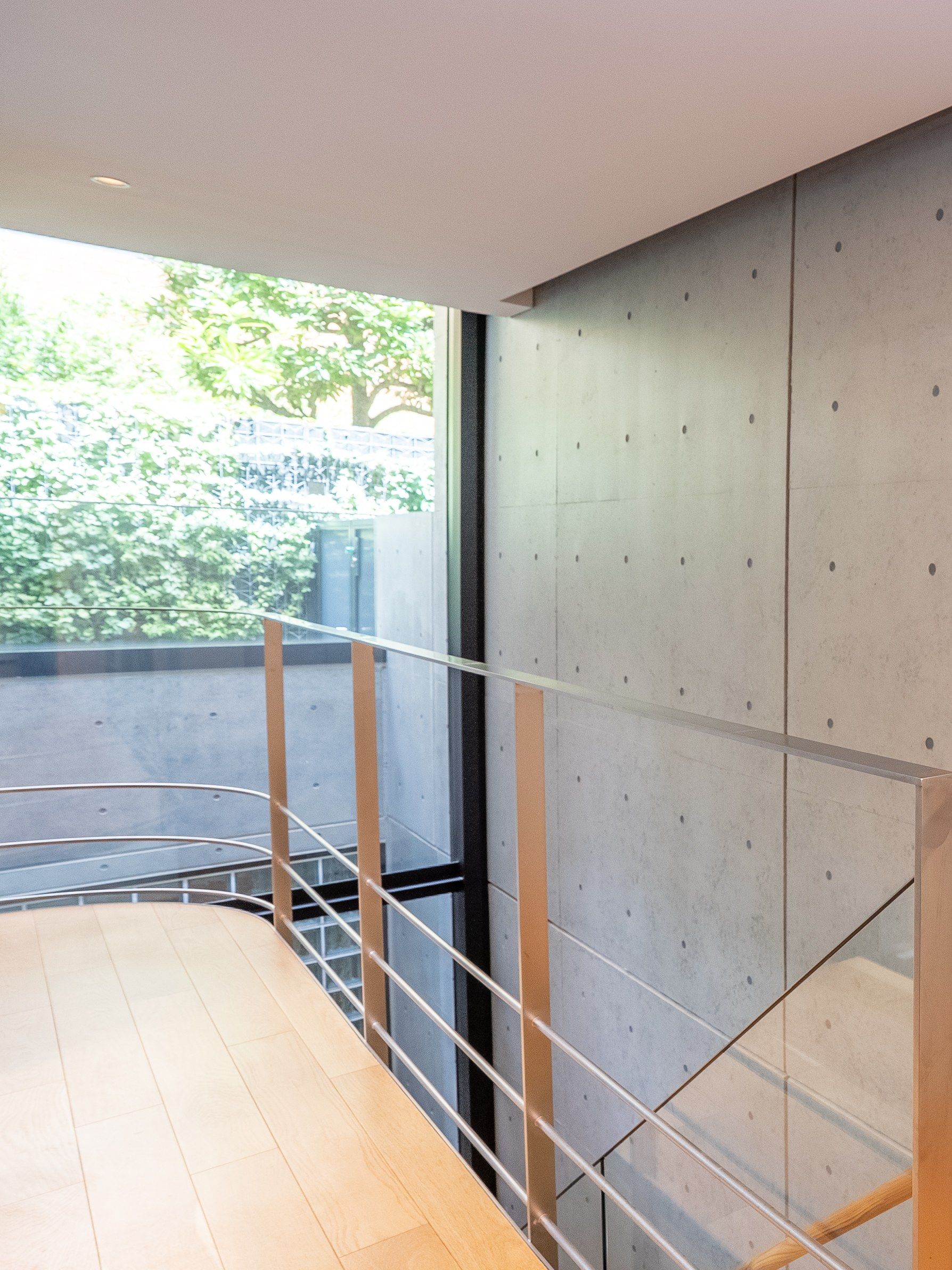 The landing rail of oak and steel beside the concrete wall, trees beyond the glass.