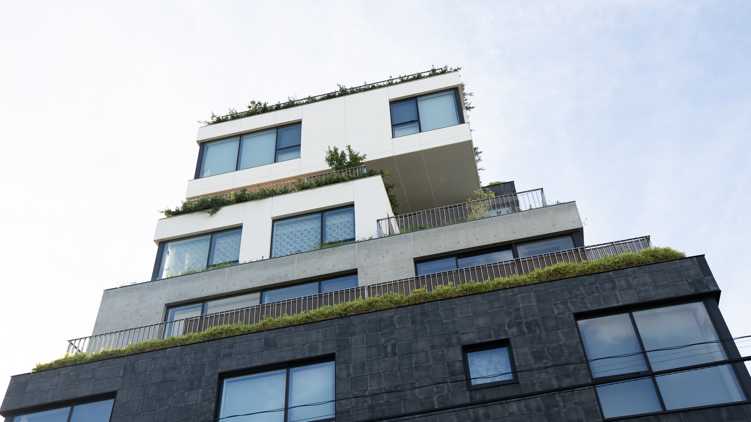 The building from the street: terraced concrete volumes stepping back under planted balconies.