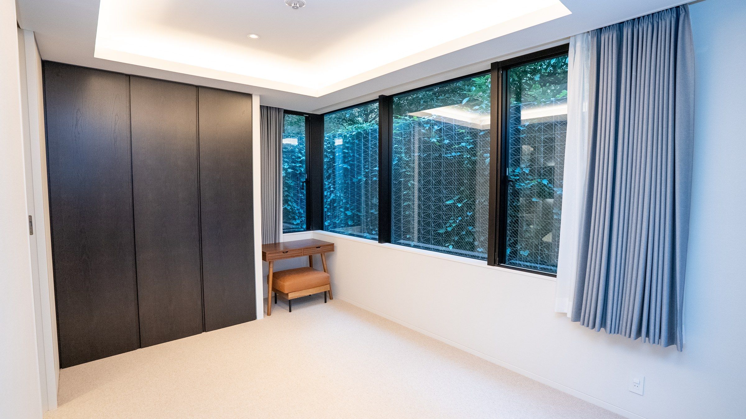A bedroom with a ribbon of windows onto the ivy wall, a writing desk beneath them.